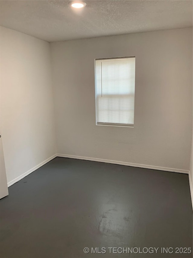 empty room with finished concrete flooring, baseboards, and a textured ceiling