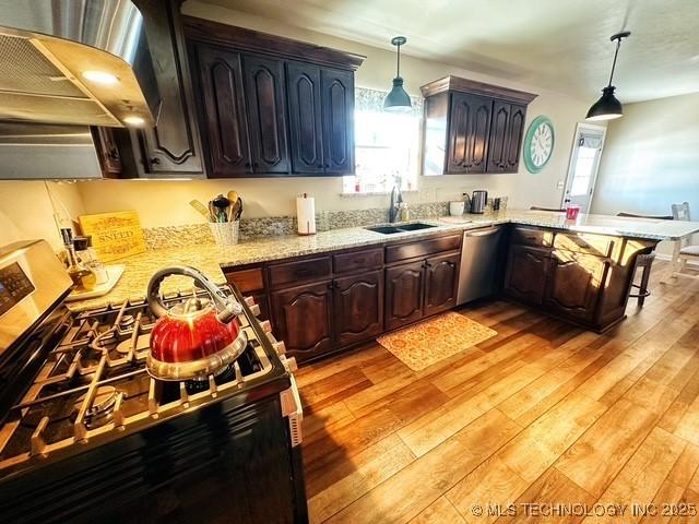 kitchen with a sink, light wood-style floors, appliances with stainless steel finishes, light stone countertops, and decorative light fixtures