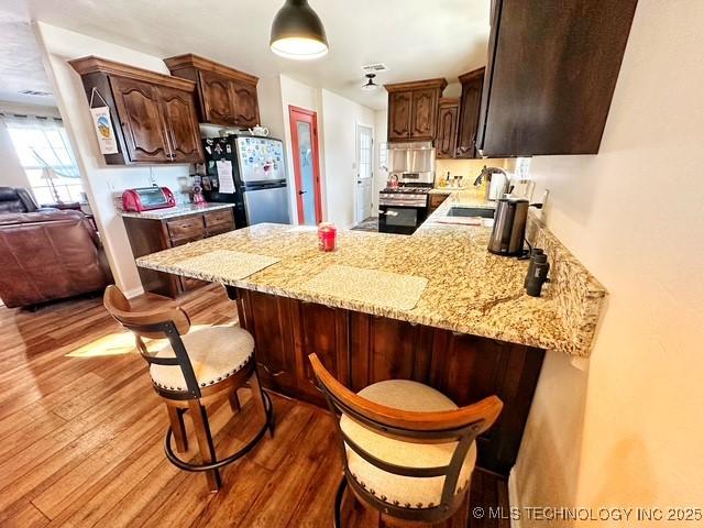 kitchen with a peninsula, appliances with stainless steel finishes, a kitchen bar, and wood finished floors