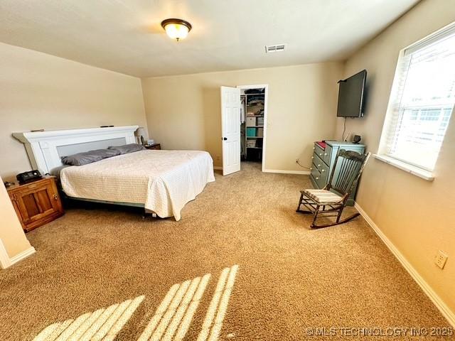 bedroom with a spacious closet, carpet, visible vents, and baseboards