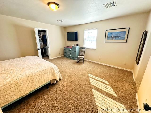 bedroom with light colored carpet, a walk in closet, visible vents, and baseboards