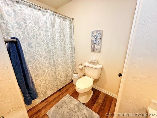 full bath featuring toilet, curtained shower, baseboards, and wood finished floors