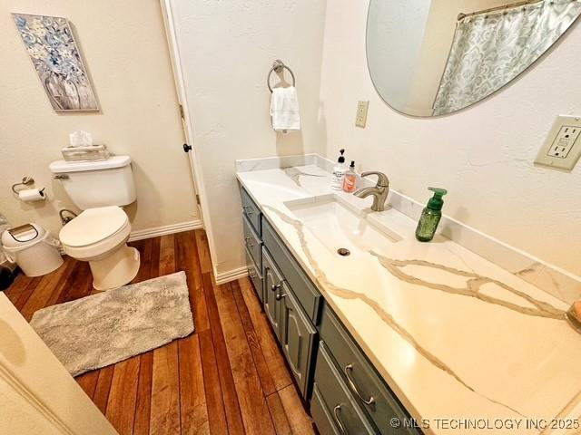 full bathroom with toilet, wood finished floors, vanity, and baseboards