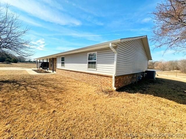 view of side of home featuring central AC, a yard, and brick siding