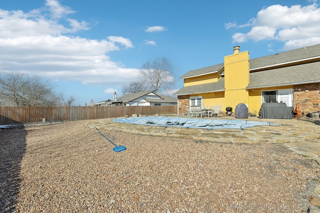 rear view of house with a patio, a chimney, stone siding, and a fenced backyard