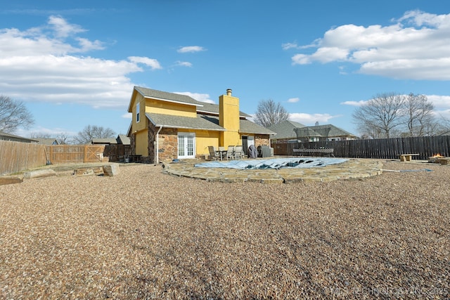 back of house with a patio area, stone siding, a fenced backyard, and a chimney