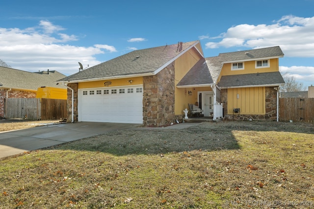 view of front of house with concrete driveway, stone siding, an attached garage, fence, and a front lawn