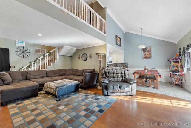 living room featuring a wainscoted wall, crown molding, a high ceiling, light wood-style floors, and stairs