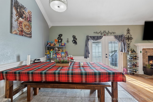 dining area featuring a warm lit fireplace, french doors, crown molding, and wood finished floors