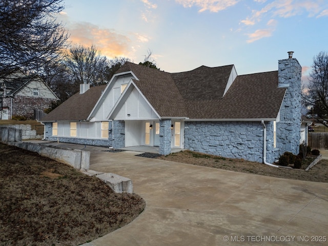 view of front of home with stone siding, a chimney, concrete driveway, and roof with shingles