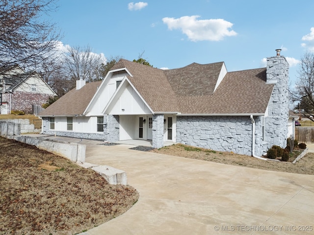 view of front of house featuring stone siding, roof with shingles, fence, and a chimney