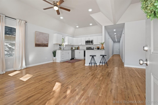 kitchen with stainless steel appliances, tasteful backsplash, light countertops, white cabinets, and a kitchen bar