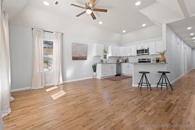 kitchen featuring light stone counters, stainless steel appliances, visible vents, white cabinets, and a kitchen bar