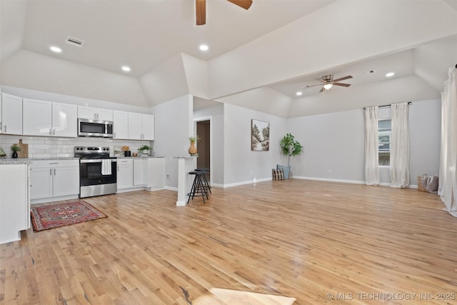 kitchen with open floor plan, tasteful backsplash, appliances with stainless steel finishes, and white cabinets