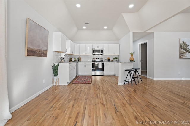 kitchen with lofted ceiling, stainless steel appliances, white cabinets, decorative backsplash, and light wood finished floors