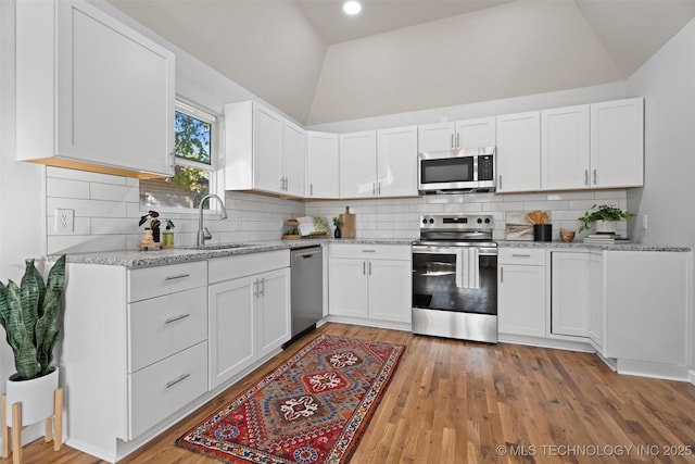 kitchen featuring lofted ceiling, white cabinetry, appliances with stainless steel finishes, and light stone counters