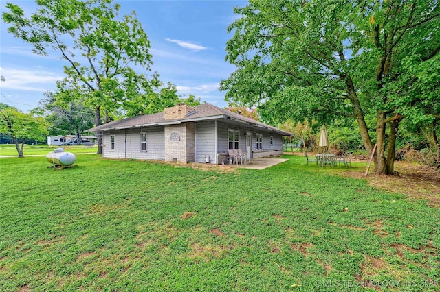 rear view of house featuring a lawn, a chimney, and a patio