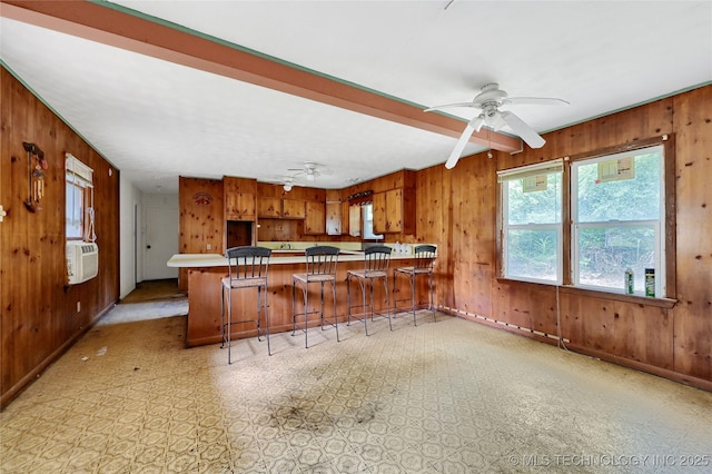 kitchen featuring wooden walls, a breakfast bar area, brown cabinets, a peninsula, and light countertops