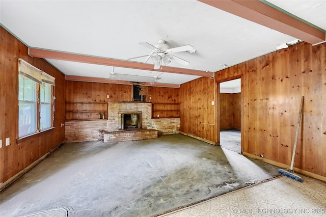 unfurnished living room with a ceiling fan, a fireplace, beamed ceiling, and wooden walls