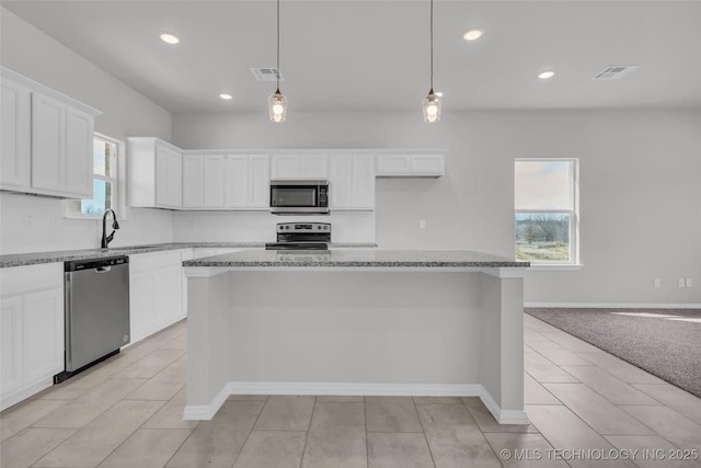 kitchen with white cabinets, appliances with stainless steel finishes, a center island, decorative light fixtures, and light stone countertops