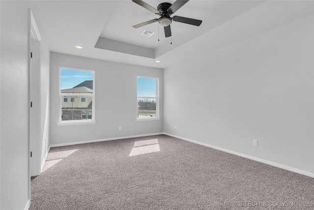 unfurnished room with ceiling fan, carpet floors, visible vents, baseboards, and a tray ceiling