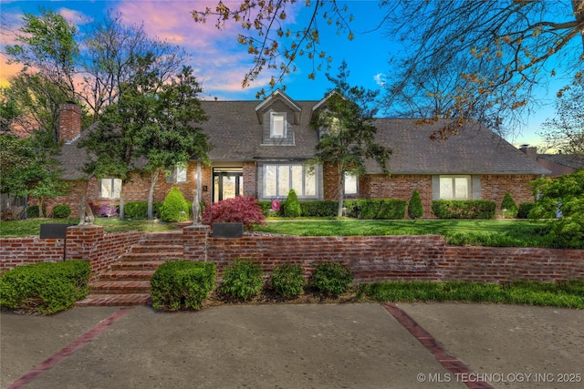 new england style home with a yard, brick siding, and a shingled roof