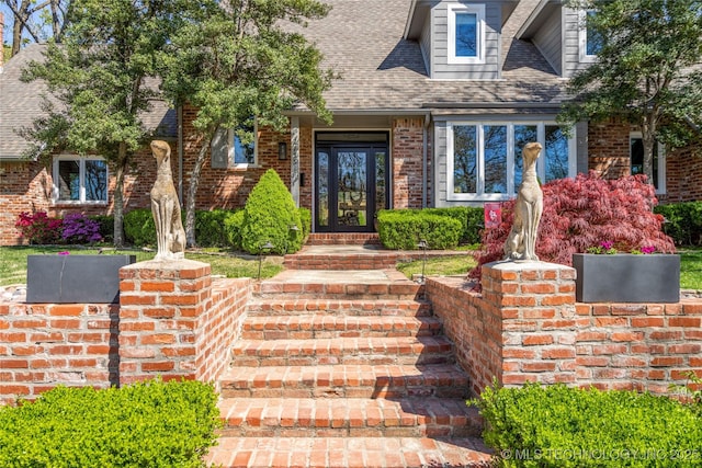 doorway to property featuring brick siding and roof with shingles