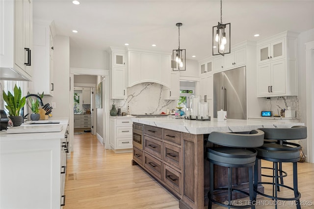 kitchen featuring light stone counters, a spacious island, glass insert cabinets, white cabinetry, and stainless steel built in refrigerator