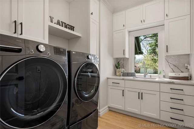 laundry area featuring light wood-style flooring, washer and clothes dryer, a sink, and cabinet space