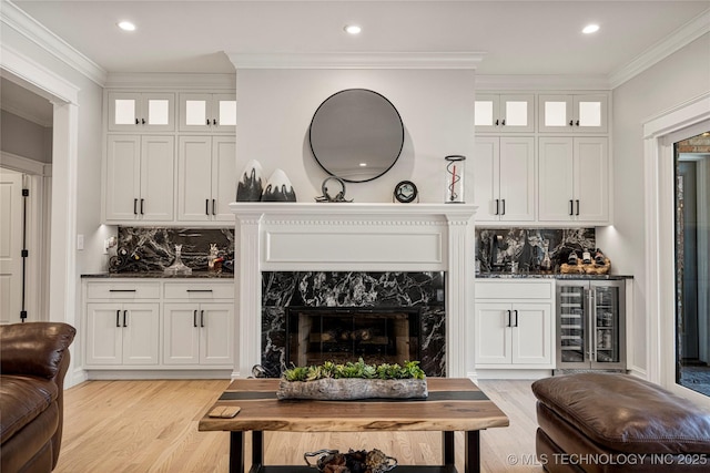 living area featuring beverage cooler, a fireplace, light wood-style floors, a bar, and crown molding