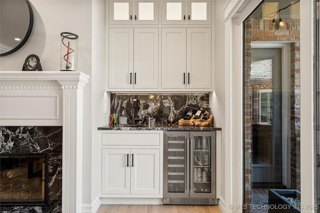 bar with light wood-style floors, beverage cooler, backsplash, and a dry bar