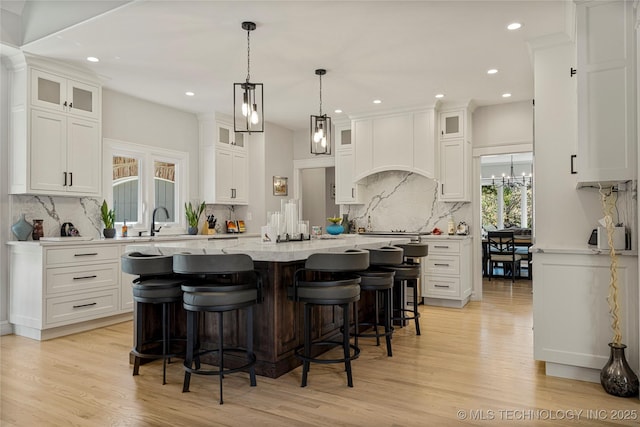 kitchen featuring custom exhaust hood, glass insert cabinets, white cabinets, and an island with sink