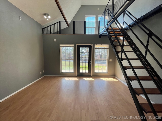 unfurnished living room with stairs, baseboards, and wood finished floors