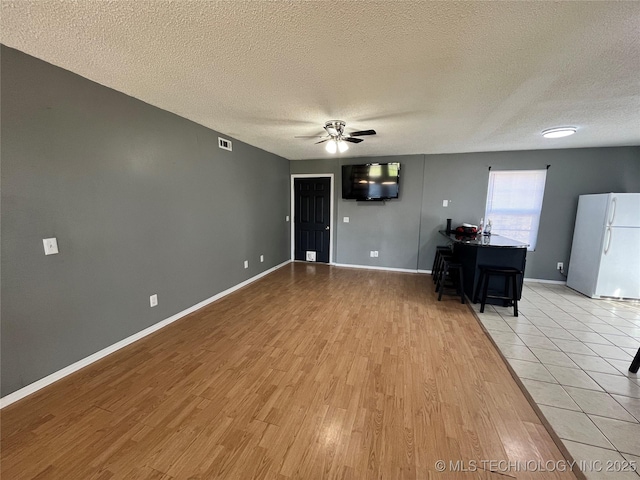 unfurnished living room featuring baseboards, visible vents, a ceiling fan, a textured ceiling, and light wood-type flooring