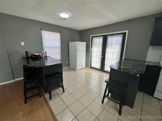 dining room with light tile patterned floors, french doors, a textured ceiling, and baseboards