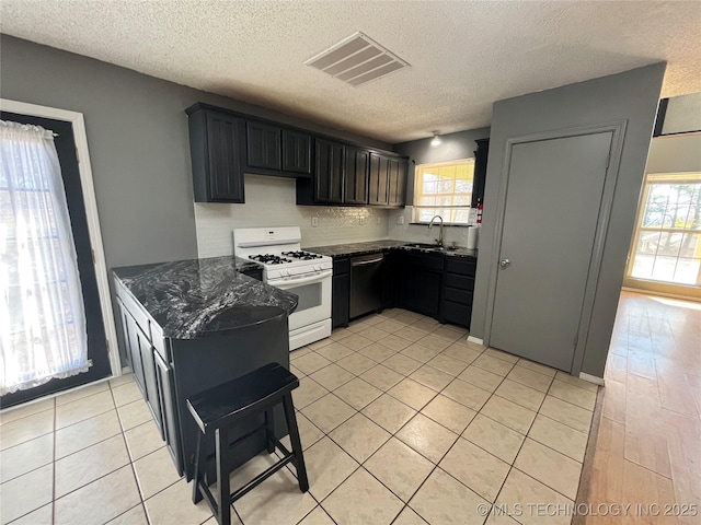 kitchen with a sink, visible vents, stainless steel dishwasher, dark stone counters, and white gas range