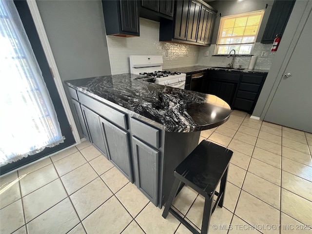 kitchen with white range with gas cooktop, a peninsula, dark stone countertops, and light tile patterned floors