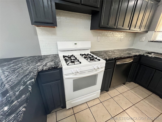 kitchen featuring light tile patterned floors, tasteful backsplash, white range with gas cooktop, dark stone countertops, and dishwasher