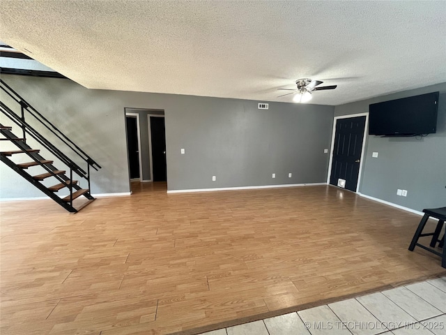 unfurnished living room with light wood finished floors, stairway, a ceiling fan, and baseboards