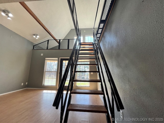 staircase featuring high vaulted ceiling, a textured ceiling, baseboards, and wood finished floors