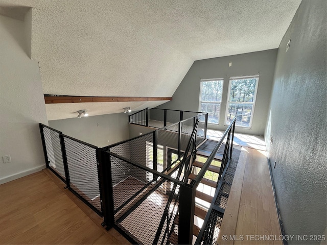 stairway featuring a textured ceiling, a textured wall, wood finished floors, baseboards, and vaulted ceiling