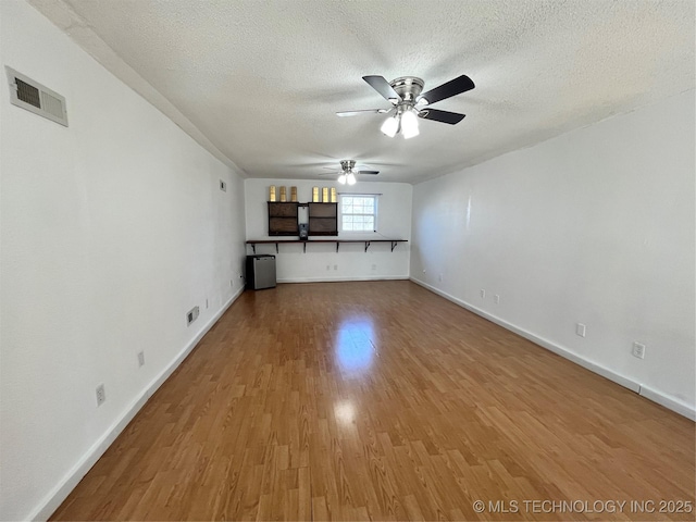 unfurnished living room featuring a textured ceiling, wood finished floors, visible vents, and a ceiling fan