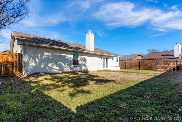 back of property with a yard, brick siding, a chimney, and a fenced backyard