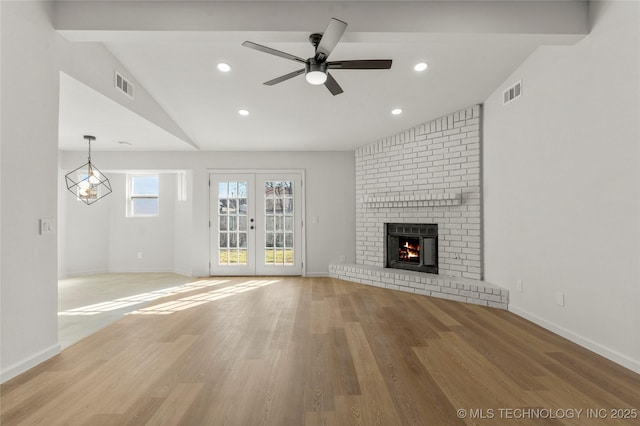 unfurnished living room featuring a fireplace, visible vents, vaulted ceiling, and french doors