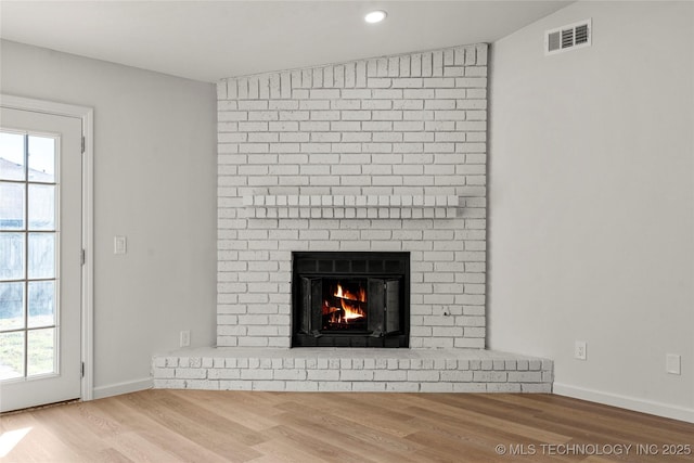 interior details with a brick fireplace, wood finished floors, visible vents, and baseboards