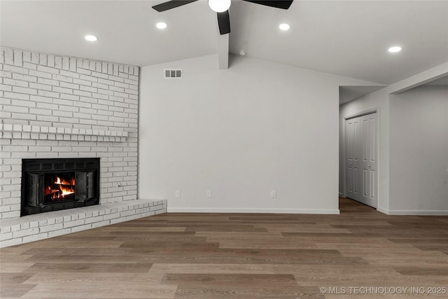 unfurnished living room featuring lofted ceiling with beams, wood finished floors, visible vents, baseboards, and a brick fireplace