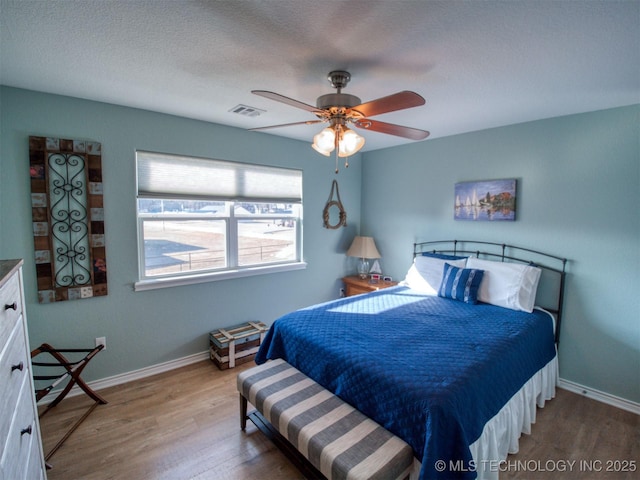 bedroom featuring visible vents, ceiling fan, a textured ceiling, wood finished floors, and baseboards