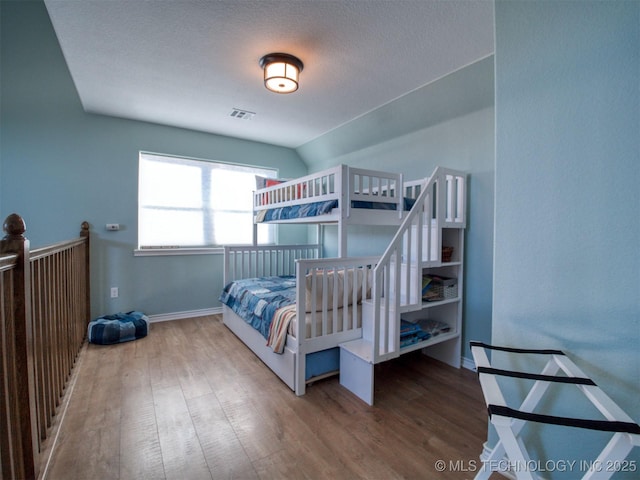 bedroom featuring visible vents, vaulted ceiling, a textured ceiling, wood finished floors, and baseboards