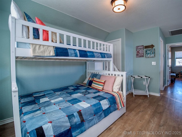 bedroom with lofted ceiling, visible vents, baseboards, and wood finished floors