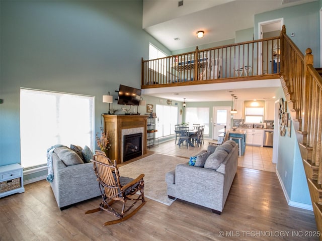 living area featuring a high ceiling, stairway, light wood-type flooring, and a high end fireplace